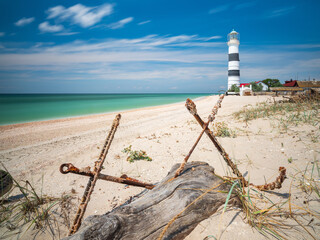 Wall Mural - wide angle view to the old lighthouse through two old anchors in summer day on the beach under blue sky with copy space