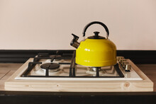 Yellow Steel Kettle On The Gas Hob On The Wooden Table. Modern Yellow Kettle On The Stainless Steel Gas Hob