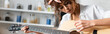 panoramic crop of curly woman playing acoustic guitar at home