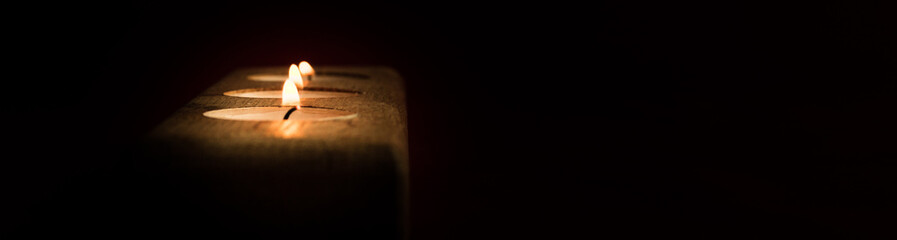 Three burning candles in wooden candle holder with copy space against dark background