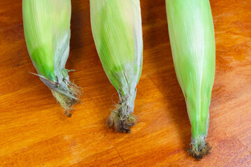 Wall Mural - fresh corn with green leaves, the crop closeup lies on a wooden table