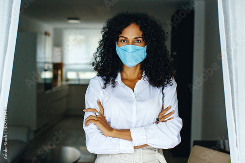 Fotomural Portrait of a woman standing indoors wearing face mask with arms crossed