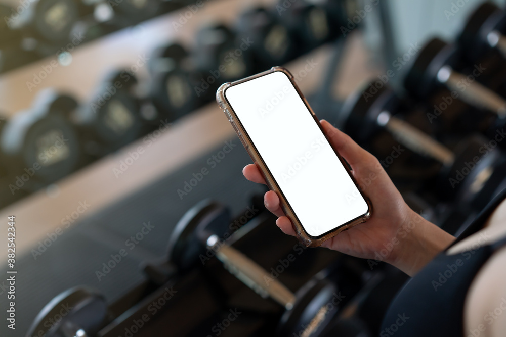 Woman hand holding mobile phone with blank white screen mockup in gym ...