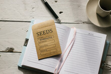 A Journal Open At A Page In April And A Packet Of Seeds Ready For Sowing
