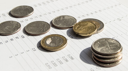 Metal coins lying on top of financial statistics paper with a set of numbers close-up light and banner