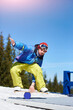 Snowboarder keeps balance on the trainer board with roller at mountains. Clear weather and sky, prepared snow. Ski season and winter sports concept