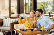 © Drazen - Happy couple having fun while using smart phone and eating cake in a cafe.