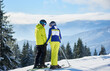 Couple of skiers on mountain edge smiling to each other. Romantic moments of spending time together during winter vacation at ski resort. Mountain panoramic landscape on blurred background. Back view.