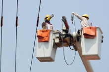 Electricians Work Together On The Electric Cable Car And Electric Pole. To Maintain The High And Low Voltage Distribution System. They Wear A Helmet With PPE Protection And Copy Space For Your Text.