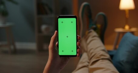 Man lying on couch using smartphone with chroma key green screen at night, scrolling through social media or online shop - internet, communications concept close up 4k template