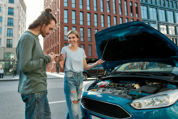 Wall Mural - Man decided to help girl with her auto, he is trying to call emergency car service while they both standing near her broken car with open hood on the city street