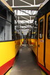 dwa rzędy żółto-czerwonych tramwajów w hali Zajezdni w Warszawie