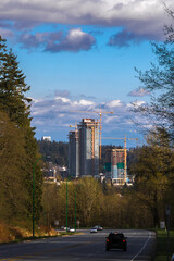 Wall Mural - Construction of high-rise buildings in Coquitlam City, construction site, construction equipment, several construction cranes  on the background of  blue cloudy sky. Forest and road with cars