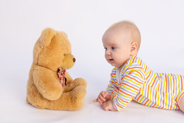 smiling baby girl 6 months old lies on a white isolated background in a bright bodysuit in front of a soft Teddy bear, space for text