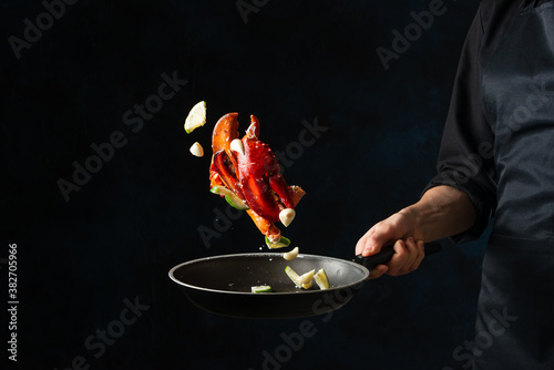 Fotomural The chef toss up king crab legs with pieces of lime in a frying pan on dark blue background