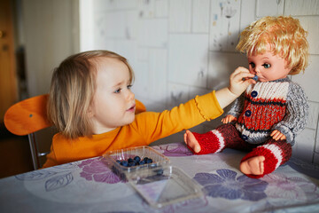 Wall Mural - Adorable toddler girl eating blueberries and feeding her doll