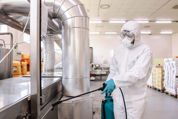 Wall Mural - Worker in sterile uniform with rubber gloves holding sprayer with disinfectant and spraying around warehouse. Corona outbreak concept.