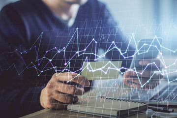 Double exposure of man's hands holding and using a phone and financial graph drawing. Analysis concept.