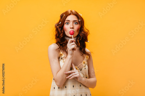 Fotomural Green-eyed girl in sundress and white choker around her neck eats lollipop