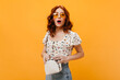 Curly girl in sunglasses confusedly looks into camera and holds small white bag