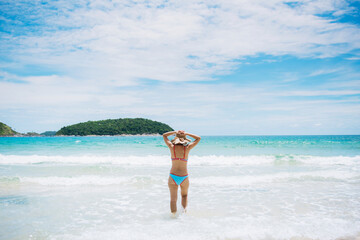 Rear view of the young asian woman in hat relaxing on the beach and looking at the sea. Travelling tour in Asia : Phuket, Thailand.