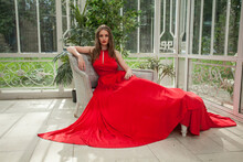 Elegant Celebrity Woman In Red Silky Dress Sitting On Vintage Armchair