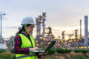 Asian woman petrochemical engineer working at night with notebook Inside oil and gas refinery plant industry factory at night for inspector safety quality control.