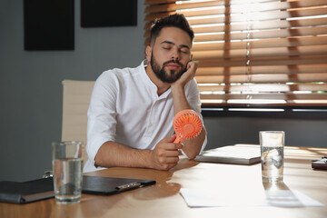 Canvas Print - Man with portable fan at workplace. Summer heat