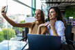 © F8  \ Suport Ukraine - Two young attractive women making selfie photos on telephone sitting in cafe space with laptop computer.