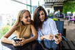 © F8  \ Suport Ukraine - Two cute women in casual clothes are looking at the screen of a mobile phone while sitting in a street cafe. Blogers are reading news on a smart-phone while having coffee break.
