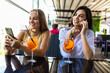 © F8  \ Suport Ukraine - Positive young women recreat together at cozy restaurant, use phones, enjoy tasty cocktails.