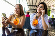 © F8  \ Suport Ukraine - Positive young women recreat together at cozy restaurant, use phones, enjoy tasty cocktails.