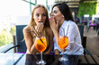 © F8  \ Suport Ukraine - Two women sharing secrets and covering faces with hands while drink cocktails in cafe.