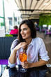 © F8  \ Suport Ukraine - Young pretty smiling woman holding the glass of Aperol Spritz cocktail in cafe