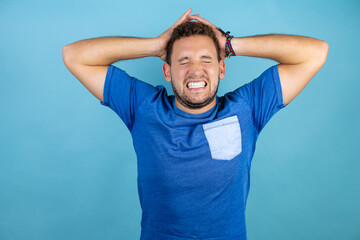 Young handsome man wearing blue casual t-shirt over isolated blue background suffering from headache desperate and stressed because pain and migraine with her hands on head