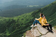 © Kateryna - Inspirational landscape. Love in the mountains. Happy couple in love sits on the edge of the cliff back to back on the big stone with an amazing mountains view on the background