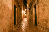 Fototapeta Uliczki - Narrow alley illuminated by street lamps at night in the old town of Dubrovnik, Croatia