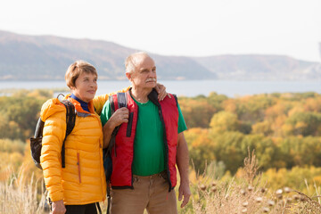 Senior couple  with backpack on a walk in an autumn nature. hyper-local travel,  family outing, getaway, natural environment
