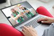 © H_Ko - Woman holds laptop on her lap and communicates in messenger in her friends with santa claus hats and protective masks. Christmas and new year during covid 19 pandemic concept.