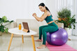 © DragonImages - Young woman training on fitness ball at home when watching tutorial on digital tablet