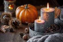 Autumn Concept Or Thanksgiving Celebration Concept With Two Lit Candles, Orange Pumpkin At The Background, Chestnuts And Pine Cones