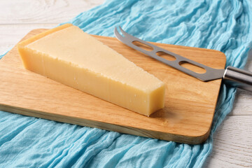 Triangular wedge of traditional italian hard cheese Grana Padano or Parmesan and cheese knife on a wood cutting boad over white wood table.