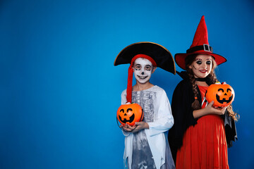 Canvas Print - Cute little kids with pumpkin candy buckets wearing Halloween costumes on blue background. Space for text