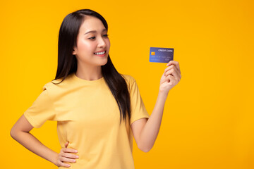 Portrait lovely young asian woman showing plastic credit card and looking at credit card, standing over yellow background. Beautiful girl get satisfied of credit card service with smile on face