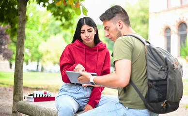 Two students studying together with a digital tablet sitting on a bench outdoor