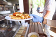 © H_Ko - Female hand in blue medical glove hold white plate with fried potatoes and stewed vegetables. Self service restaurant with tray.