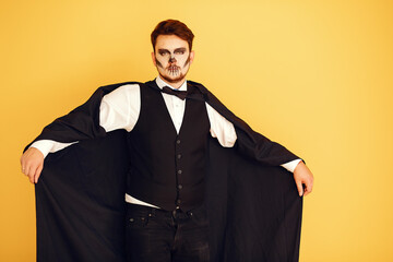 Wall Mural - Portrait of man on yellow background. Halloween skull make up showing his emotions.