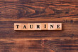 Taurine word lettering made of wooden cubes on dark rustic wooden background. Taurine helps to improve energy metabolism in the body. Bodybuilding food supplements concept.