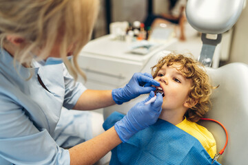 Wall Mural - Cute young boy visiting dentist, having his teeth checked by female dentist in dental office.