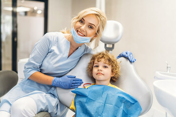 Wall Mural - Cute young boy visiting dentist, having his teeth checked by female dentist in dental office.